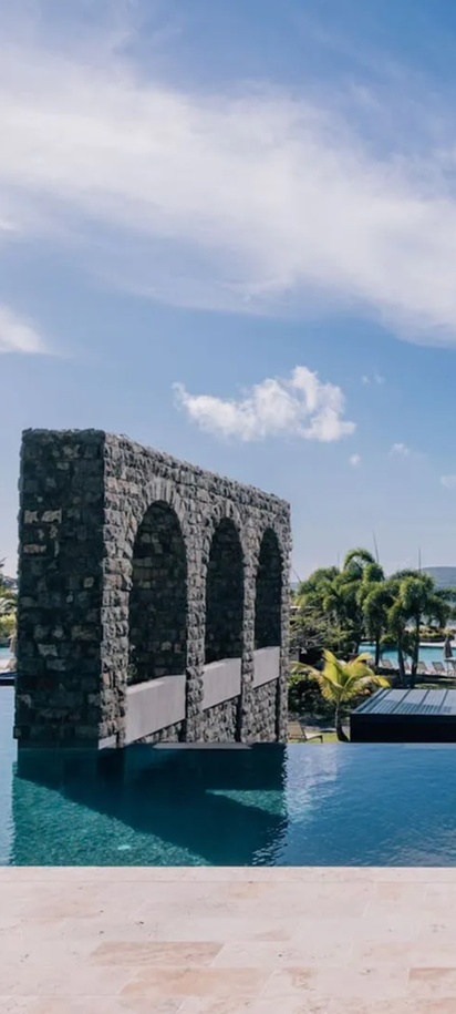 view of the pool and iconic stone archways at the Park Hyatt St. Kitts Christophe Harbour hotel, located on Banana Bay