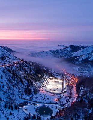 a nighttime panoramic view of Almaty, Kazakhstan, with the Zailiysky Alatau mountains in the background