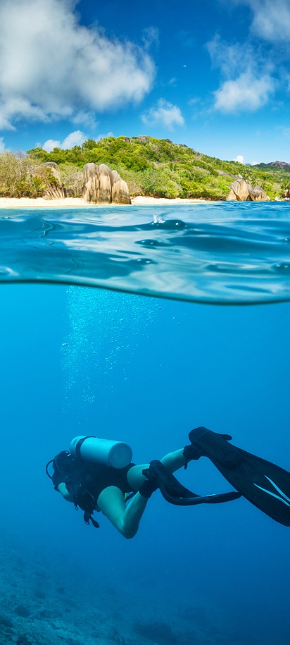 split-view underwater shot of scuba divers exploring the clear turquoise waters of the Seychelles archipelago in the Indian Ocean