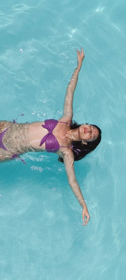 a woman in a purple bikini floating peacefully in a clear swimming pool of the Sunprime Kamala Beach Resort in Phuket, Thailand
