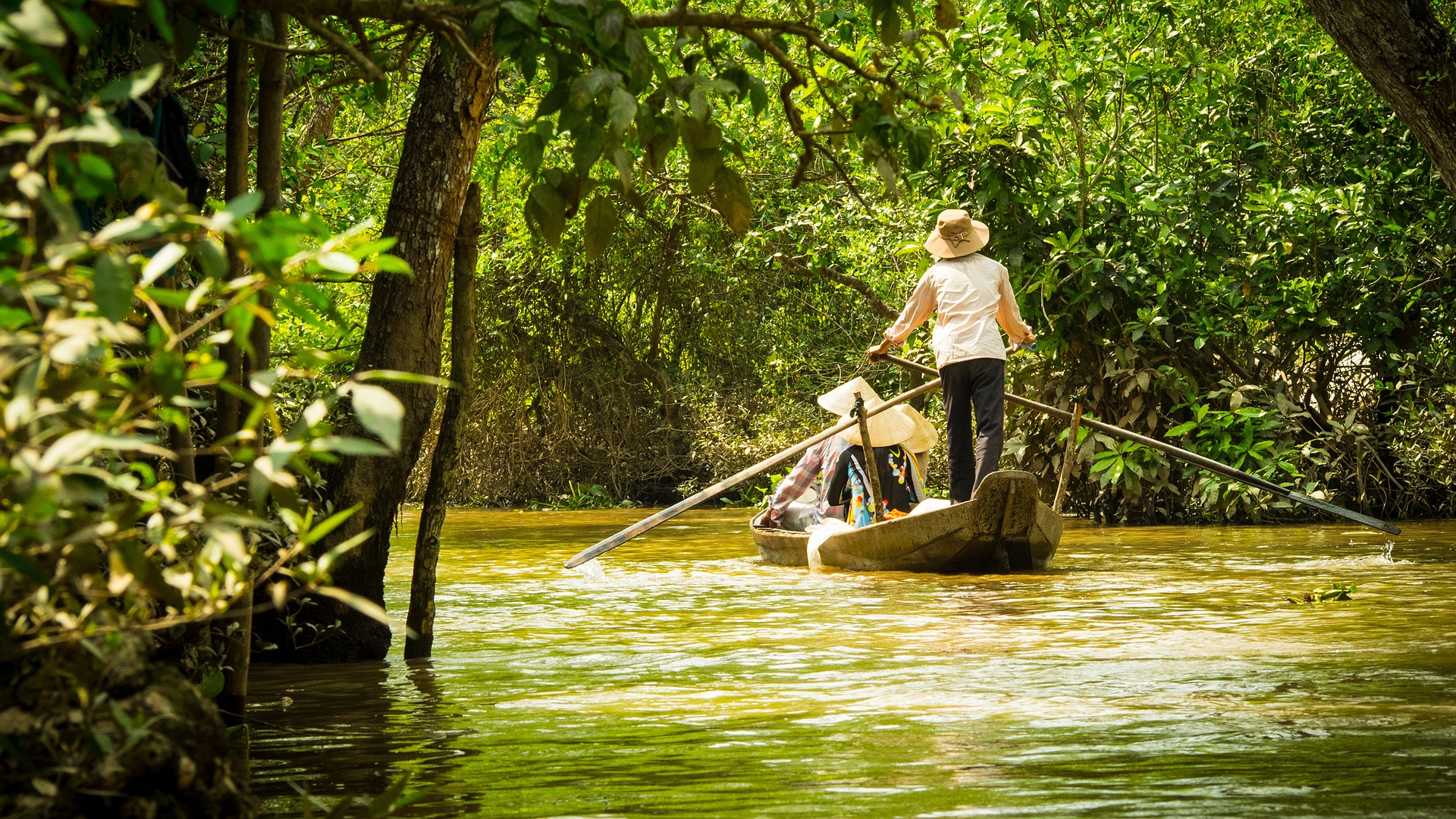 traditional wooden sampan boat in a narrow, lush canal of the Mekong Delta, Vietnam