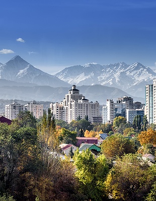 a nighttime panoramic view of Almaty, Kazakhstan, with the Zailiysky Alatau mountains in the background