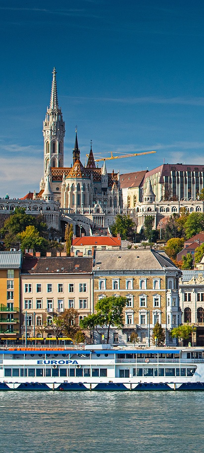 a scenic view of Budapest, Hungary, specifically featuring the Danube River with boats and the Buda side skyline