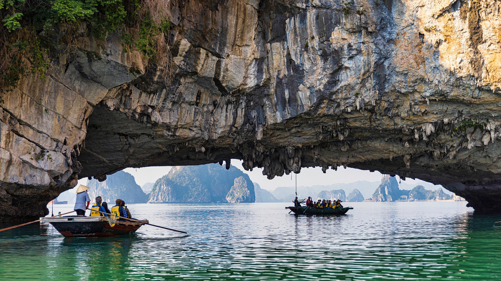  a boat tour passing through a natural archway at Bai Tu Long Bay in Vietnam